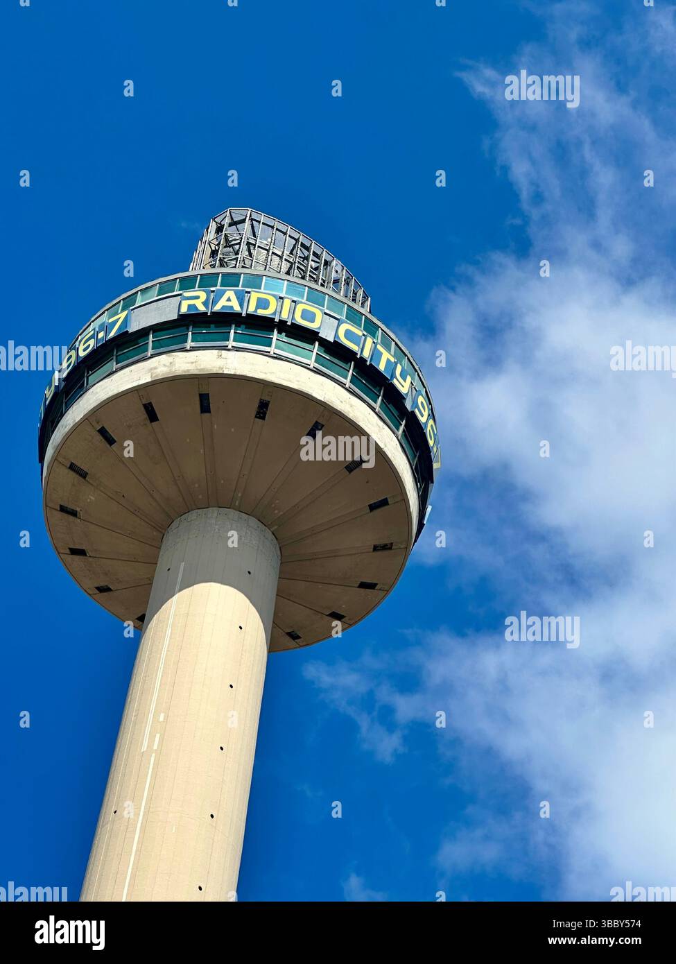 Looking up at Radio City Tower, Liverpool, blue sky and fluffy clouds above. The circular top contrasts with the concrete base in this iconic view. - Smartphone Captured Stock Image