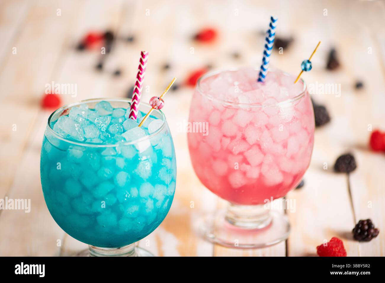 Glasses with ice filled with raspberry and blackberry soda with blueberries, on a white wooden table. Stock Photo
