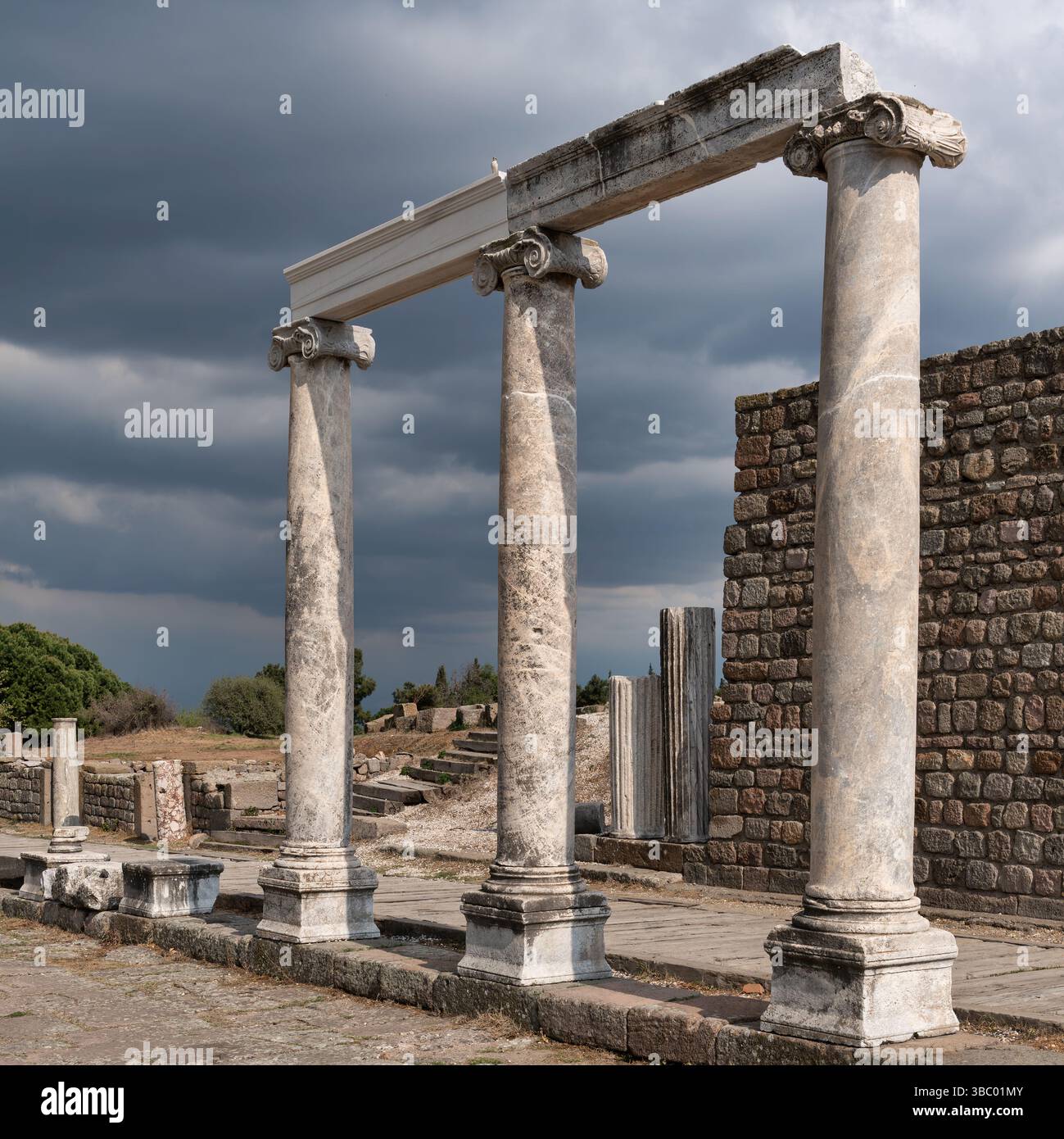 Ancient Ionic columns at the Acropolis of Pergamon ruins under a dark, cloudy sky. Bergama, Turkey Stock Photo