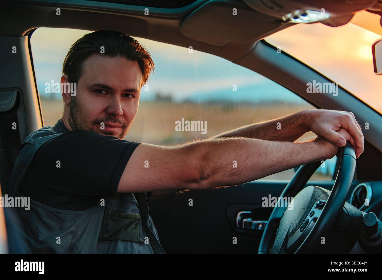 Handsome young man driving car at sunset Stock Photo