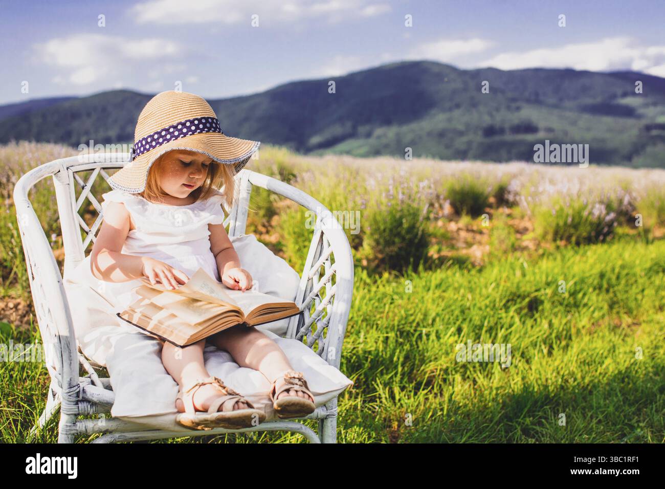 Cute little girl in a white dress and hat sitiing on the chair at the ...