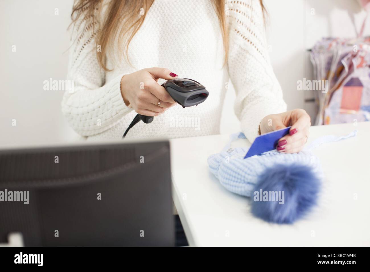 Female seller scanning winter hat at store Stock Photo
