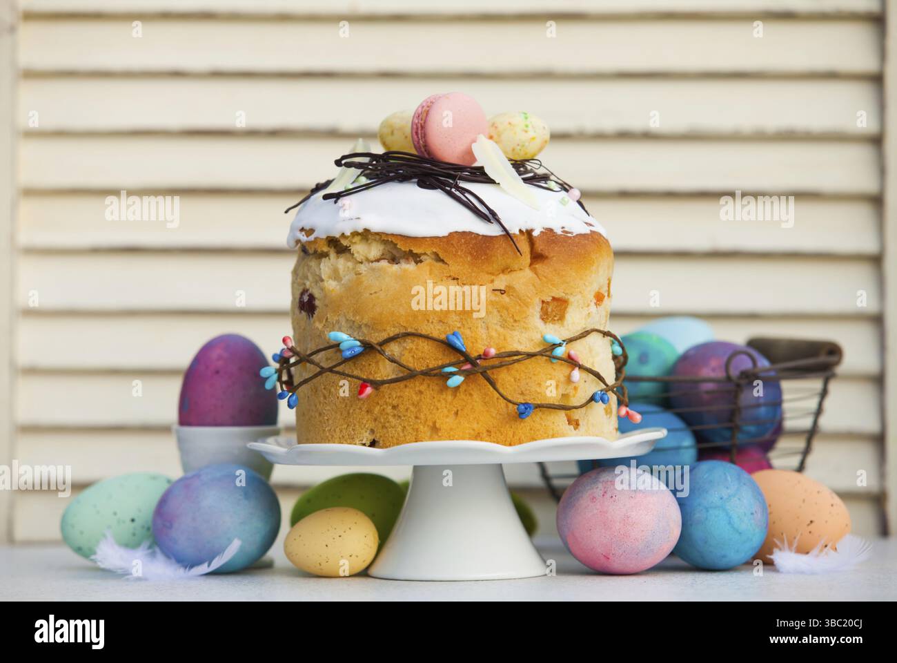Professionaly baked traditional Easter bread - paska with stylish decoration on top. Multicilor eggs around cake stand with Easter bread on it. Spring Stock Photo