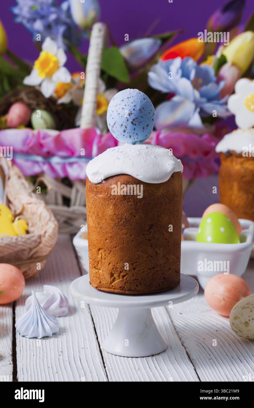 Close-up small traditional Easter breads, glazed and decorated for children with ginger breads in chicken shape. Basket with bright colorful flowers o Stock Photo