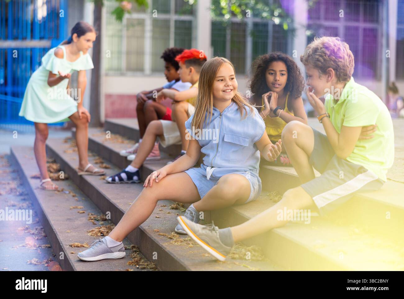 Positive tweenagers friendly blabbing while sitting on steps outdoors Stock Photo