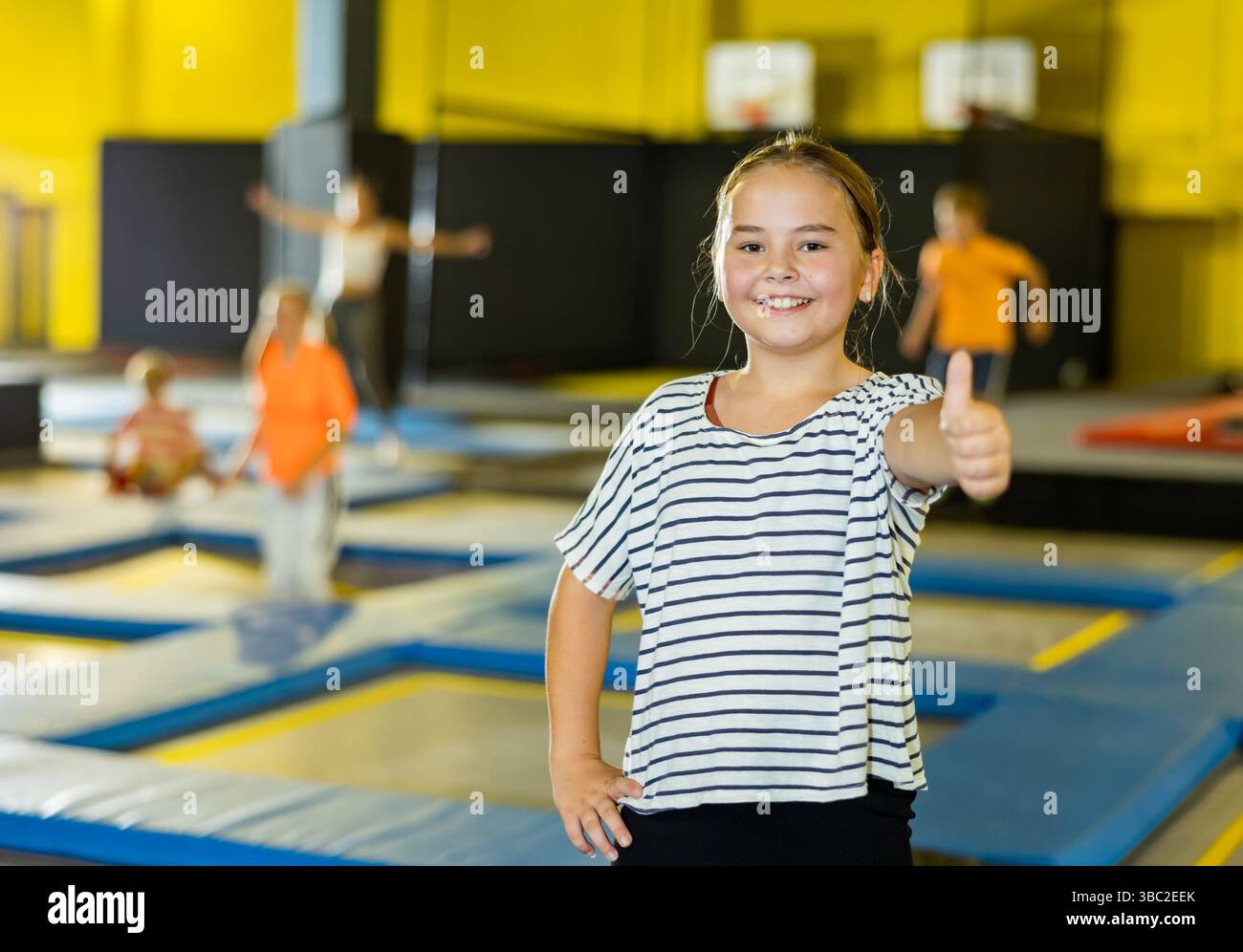 Cheerful tween girl giving thumbs up on trampolines in inflatable ...