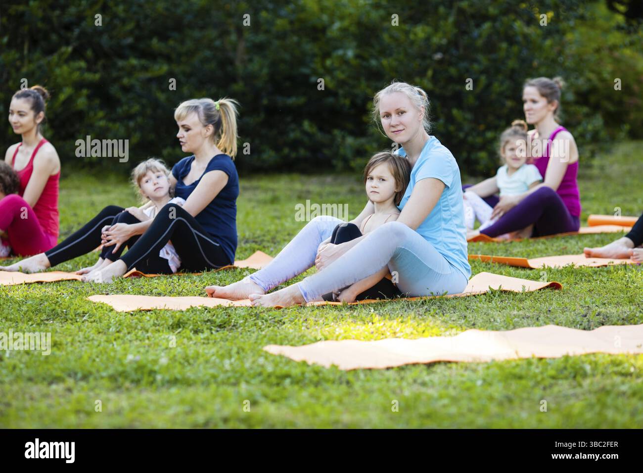 Group of mothers and their children doing exercise practicing yoga on a ...