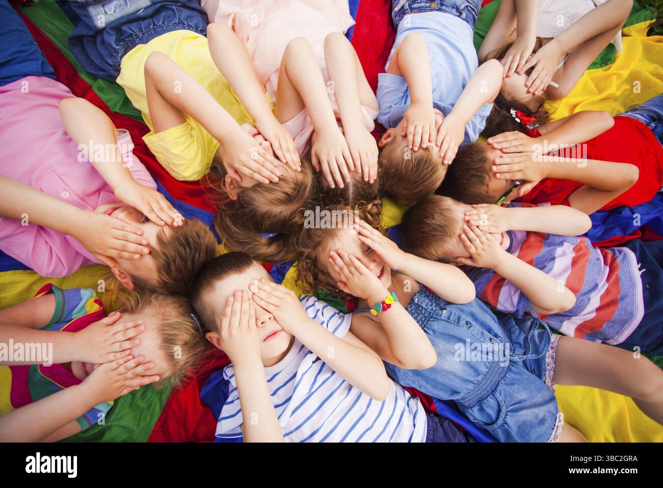 Top view children covering faces by hands, laying on a floor very closely, touching their heads and hair. Kids trying to relax after active games Stock Photo