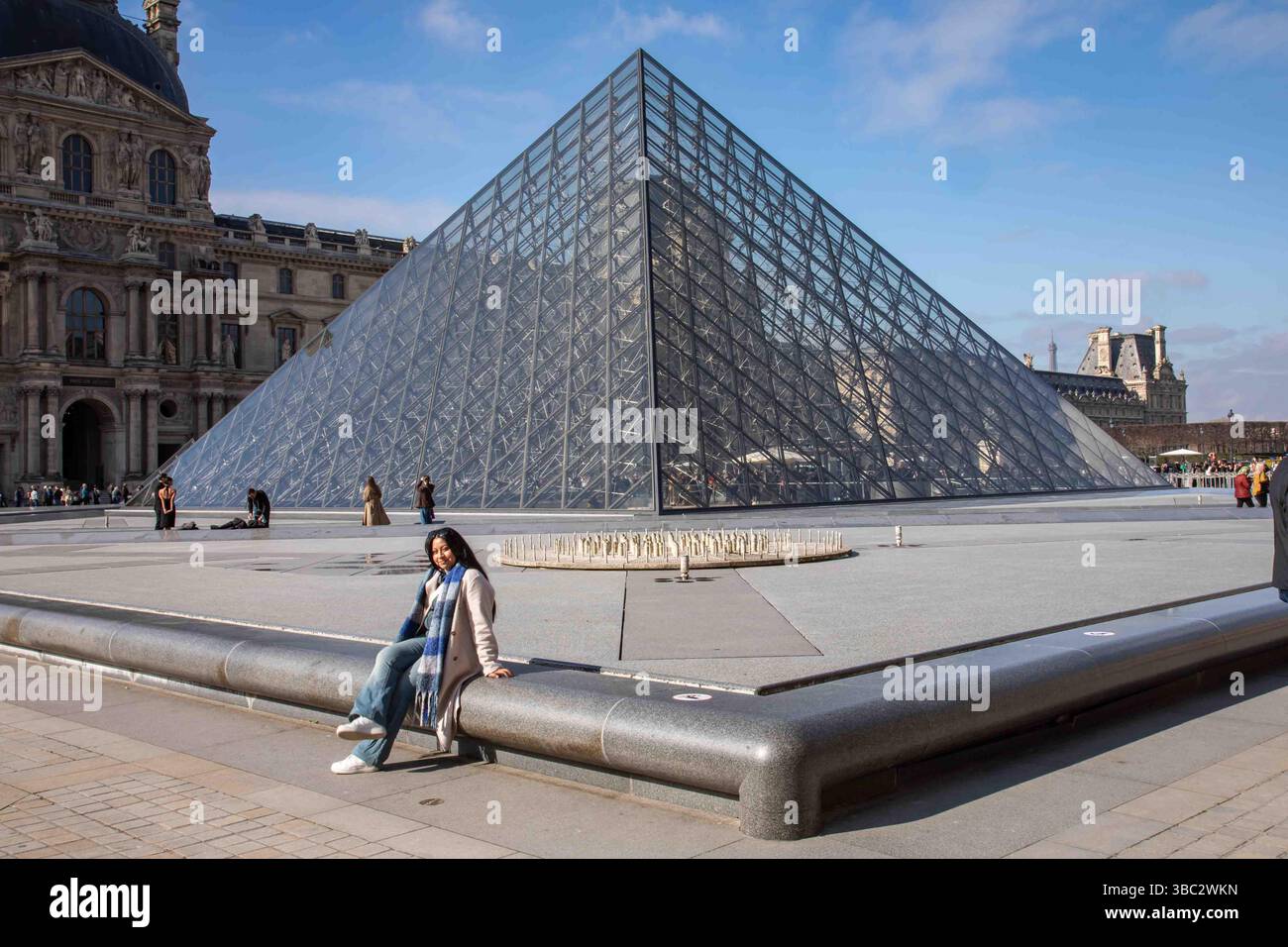 Woman sitting by Louvre Museum glass pyramid skylight in Napoleon Courtyard. Paris, France. Stock Photo