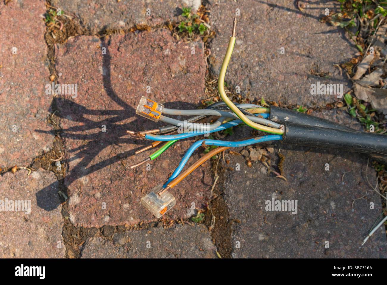 Frayed electrical cables exposed on rustic brick pavement. Colorful ...