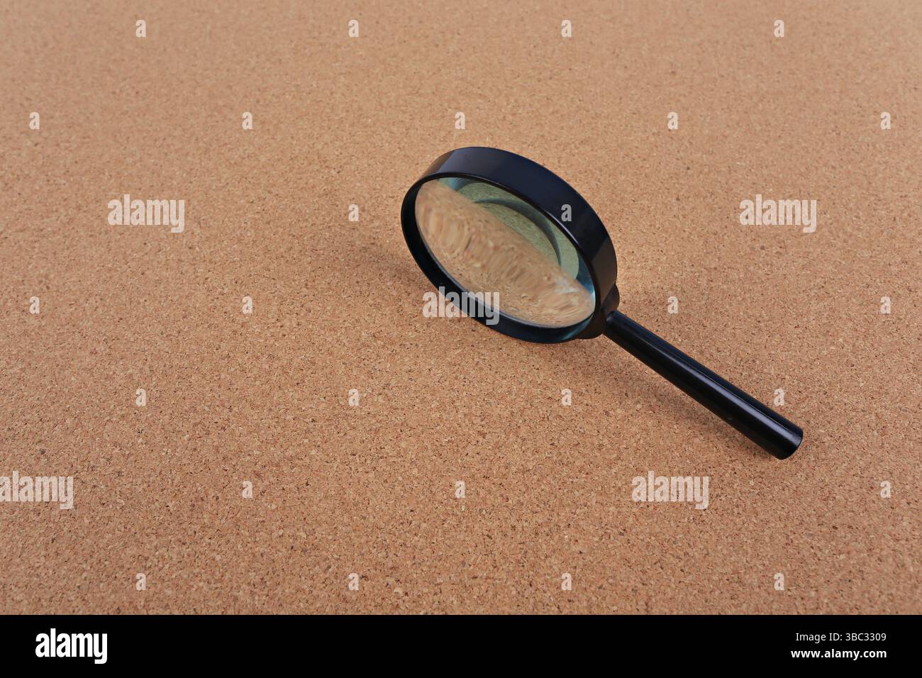 Magnifying glass placed on a cork board background. Idea for searching, detective work or typing text Stock Photo