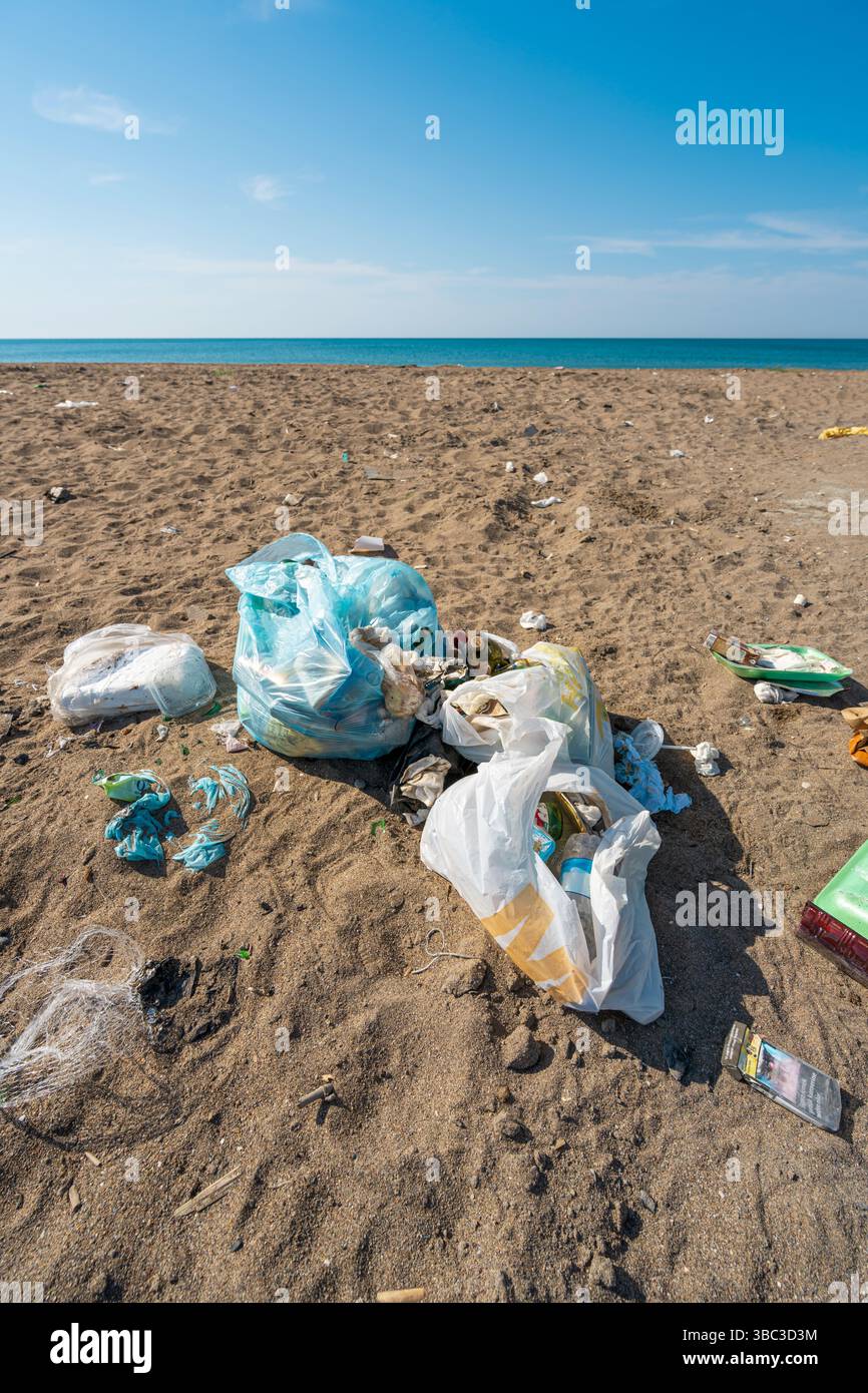 Plastic bags and bottles littered on a sandy beach by the sea Stock Photo
