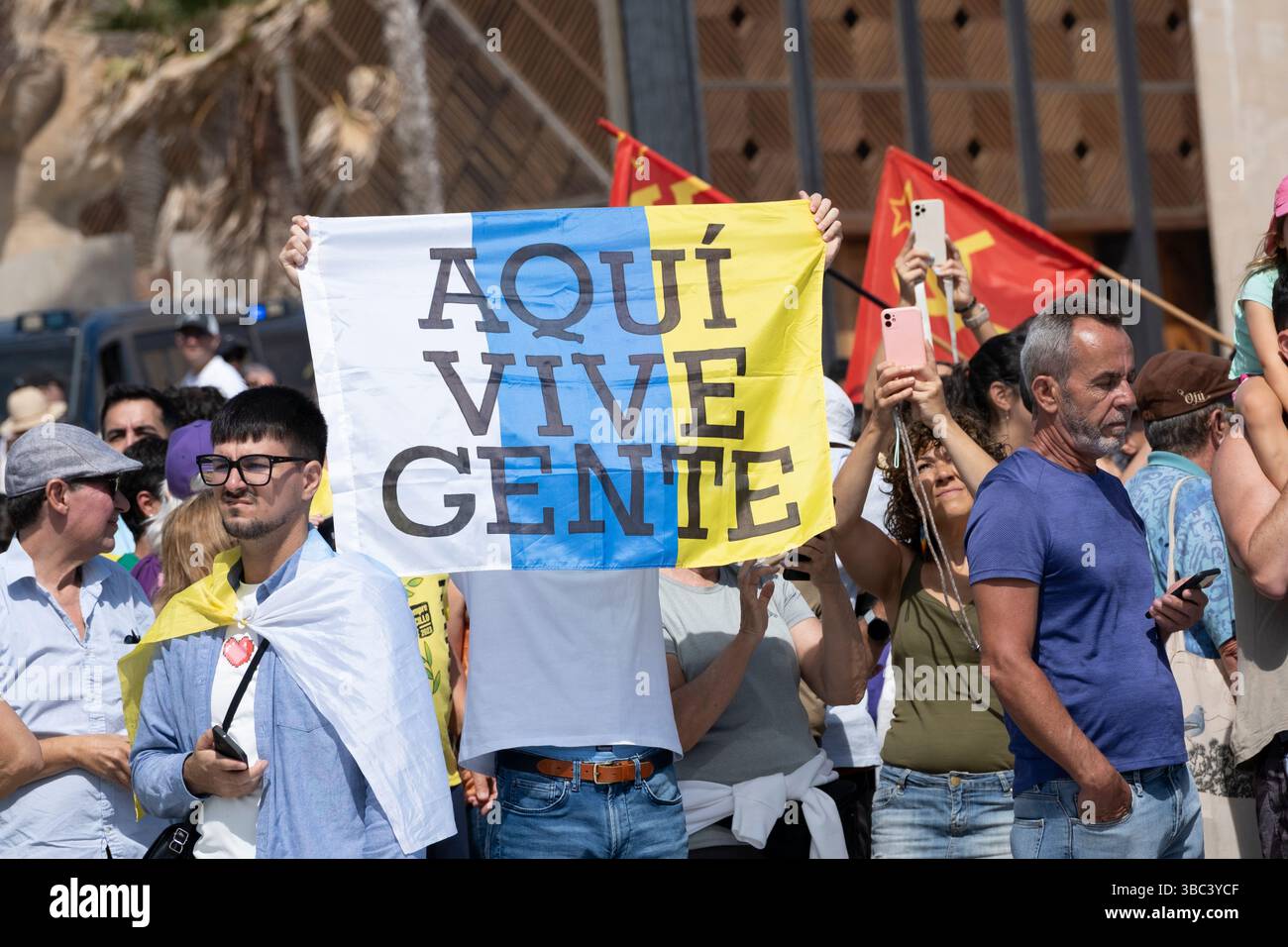 Gran Canaria, Canary Islands, Spain, 18th May 2025. Thousands of locals march along the seafront overlooking the city beach in Las Palmas, the capital of Gran Canaria. One of many protests throughout the Canary Islands calling for a freeze on tourist numbers and a more sustainable tourism policy. Holiday rental homes are also making it difficult for some locals to afford to rent property. PICTURED: A man holds a Canary Islands flag saying; people live here. Credit: Alan Dawson/Alamy Live News Stock Photo