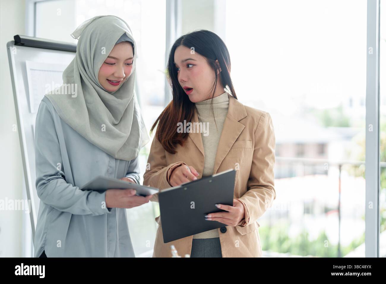 Two young Asian businesswomen collaborate in a modern office ...
