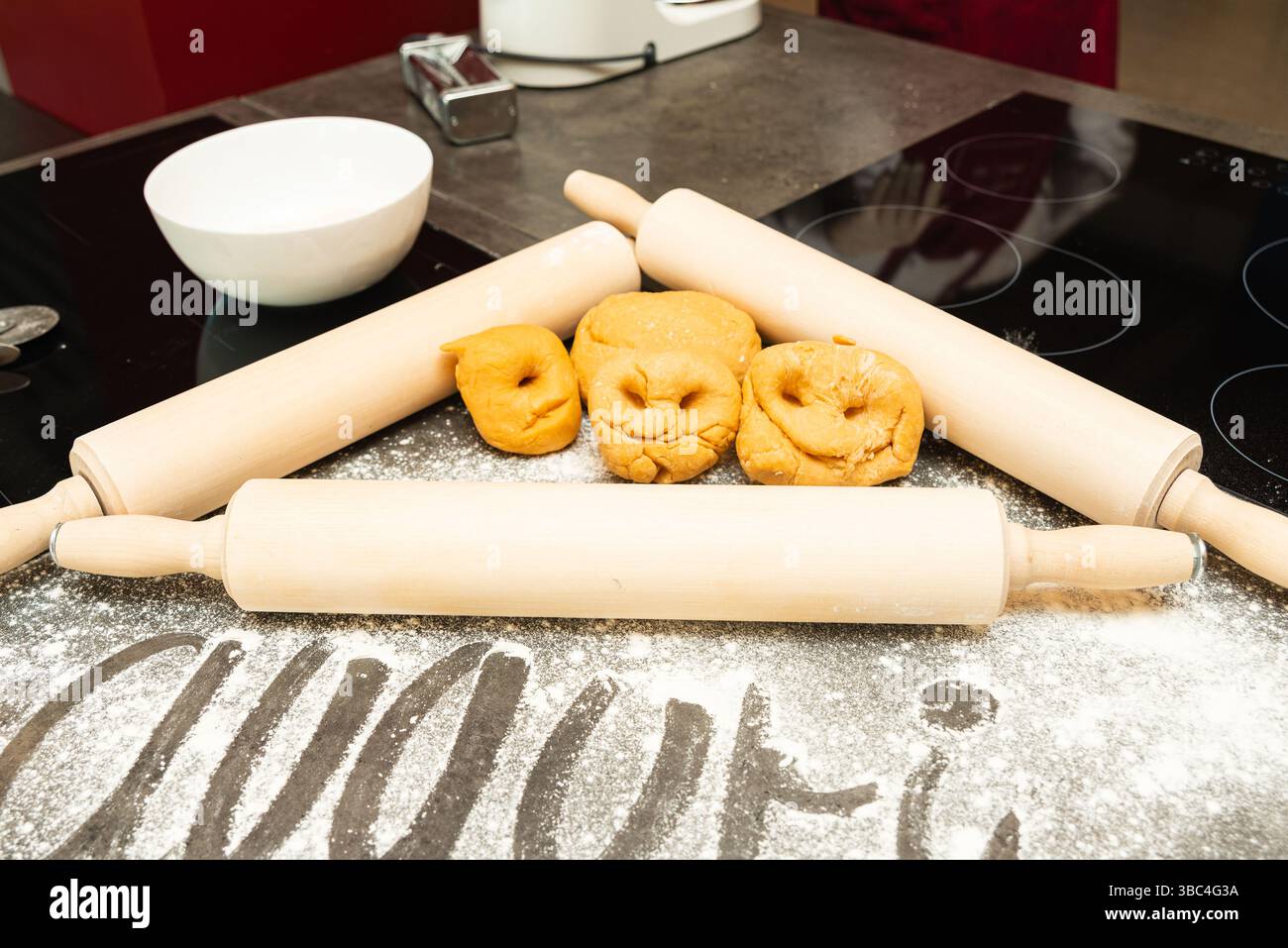 Funny dough balls shaped into smiley faces surrounded by rolling pins on a floured kitchen surface during baking preparation. Stock Photo