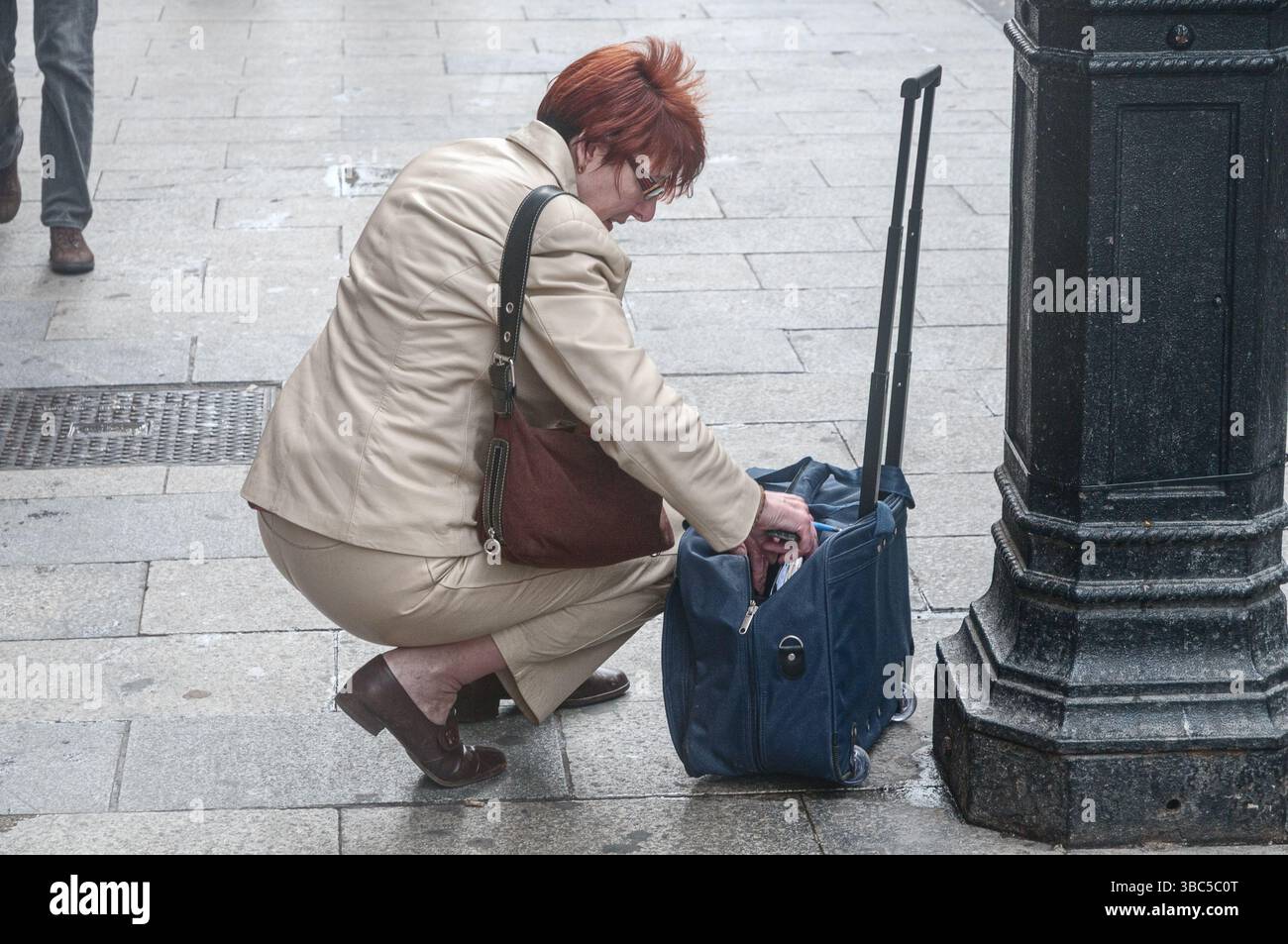 A business woman crouches in the street to search for something in her ...