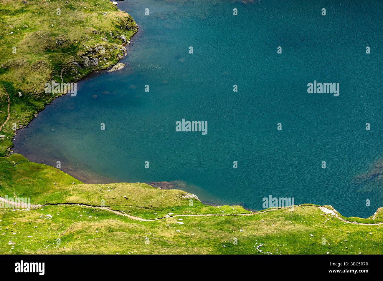capra lake of fagaras ridge in summer. rippled water surface and grass on the shore view from above. popular attraction. alpine pond carpathian mounta Stock Photo