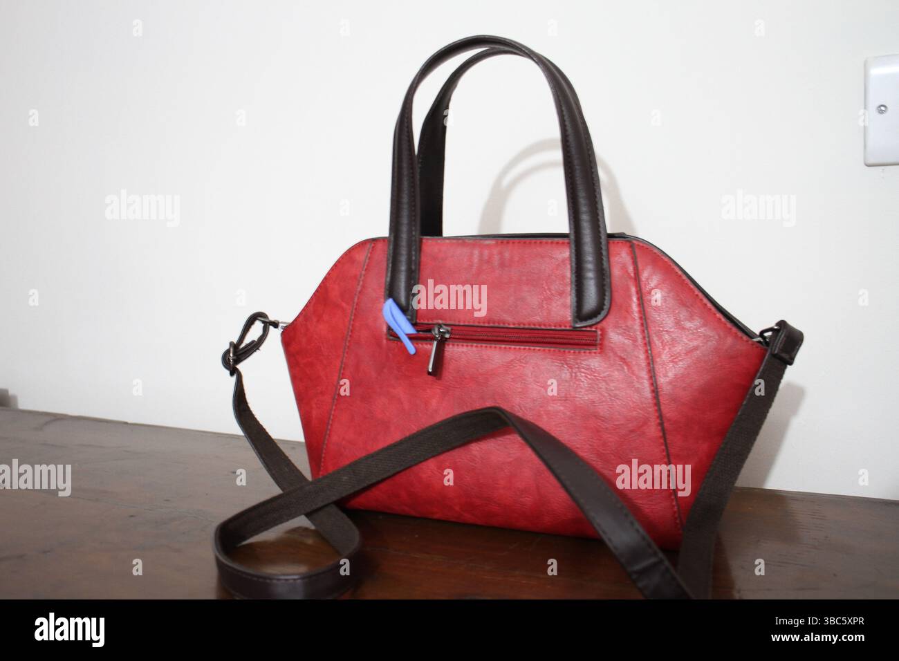 A red colored handbag is on the wooden surface with a blue pen. Stock Photo
