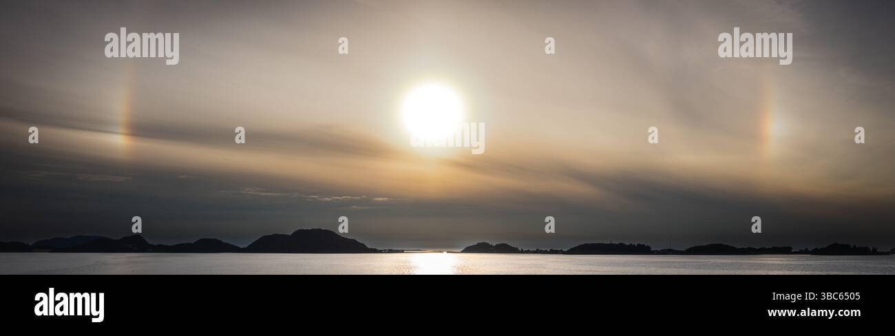 Parhelia (sundogs) appear at sunset over coastal Norway, caused by sunlight refracting through ice crystals in the atmosphere. Stock Photo