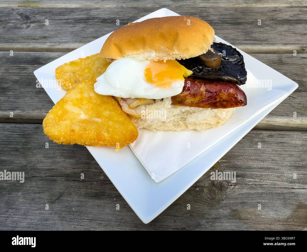 A breakfast bun sandwich containing bacon, sausage, egg, mushroom and potato hash browns. - Smartphone Captured Stock Image