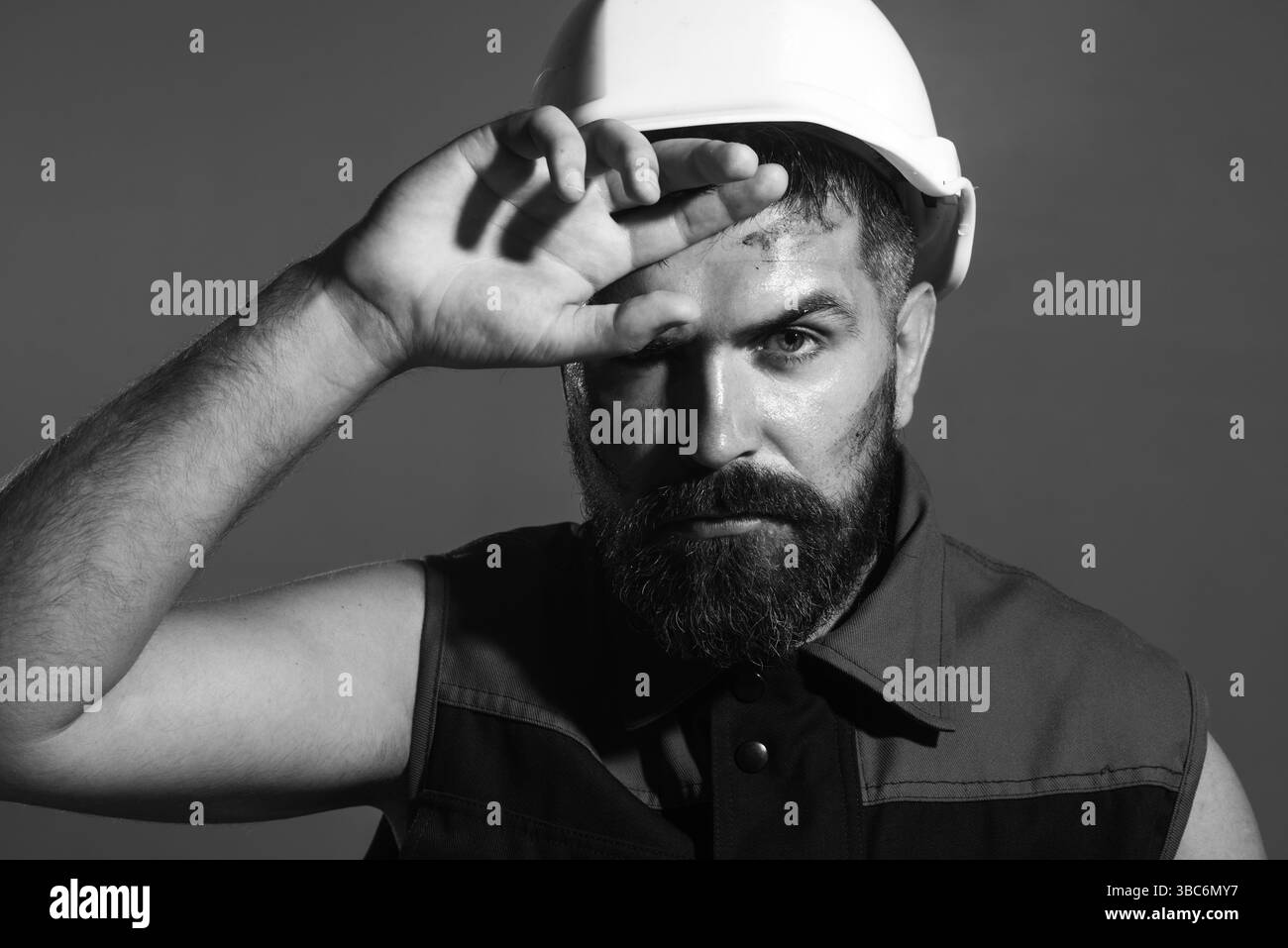 Hard work at construction site. Closeup portrait of tired heavy industry engineer or builder in safety helmet wipes sweat from forehead. Fatigued male Stock Photo