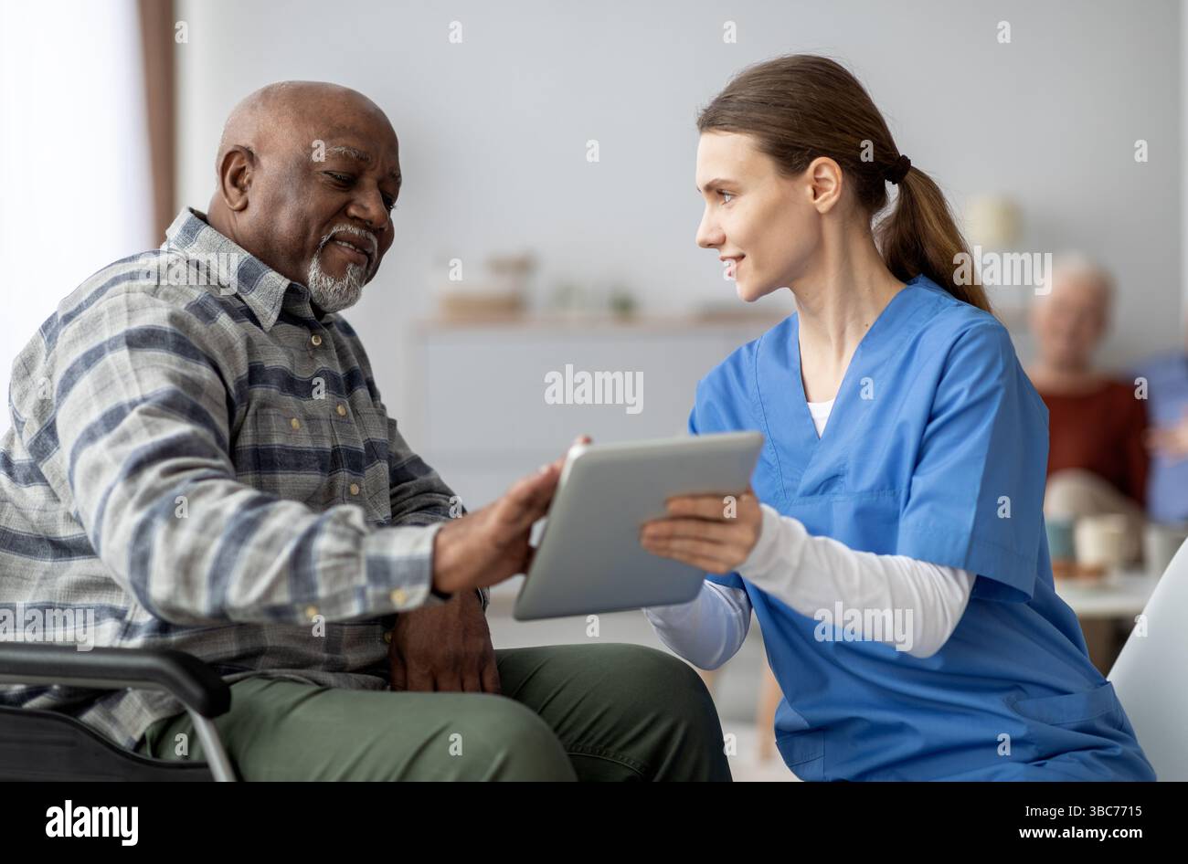 Friendly nurse helping black senior man using digital tablet Stock Photo