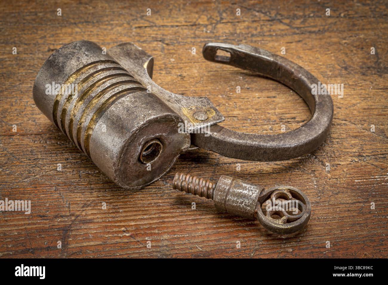 Vintage round shape hand crafted screw type iron padlock (unlocked) with a key on rustic wood Stock Photo