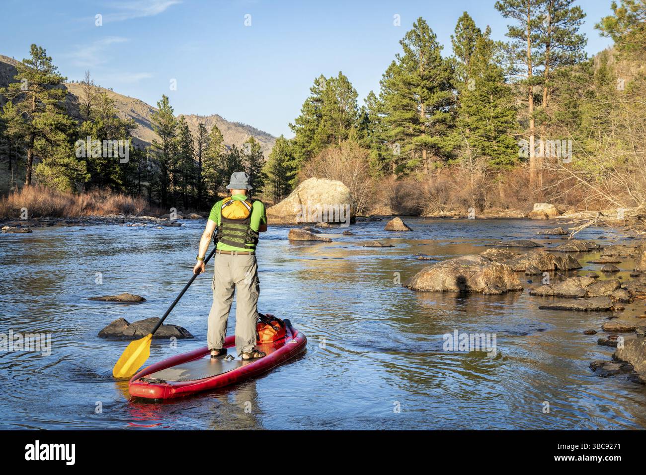 Senior male paddling inflatable stand up paddleboard through rock ...