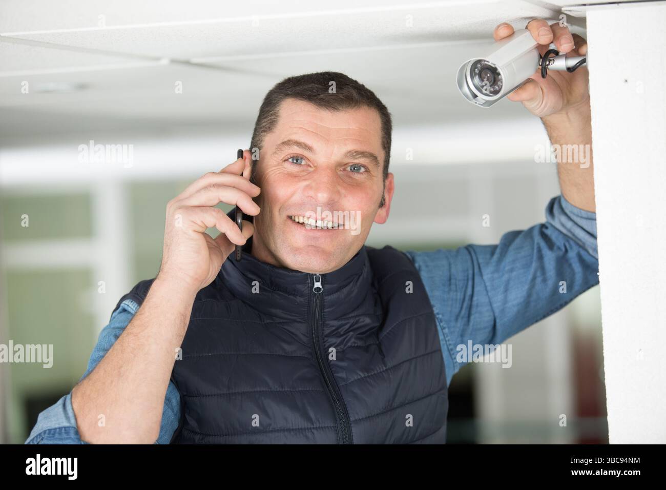 smiling contractor by cctv camera using smartphone Stock Photo