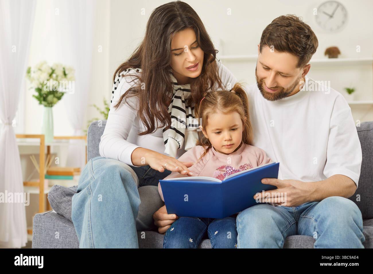 Close loving family at home, couple of parents teaching cute kid girl, read book, watching pictures Stock Photo