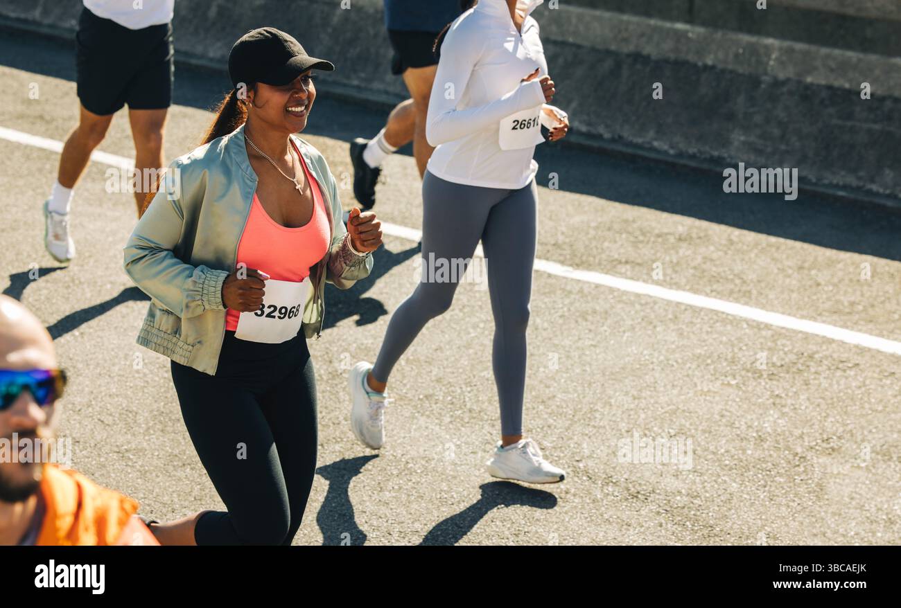 A cheerful female runner is seen smiling while participating in a road ...