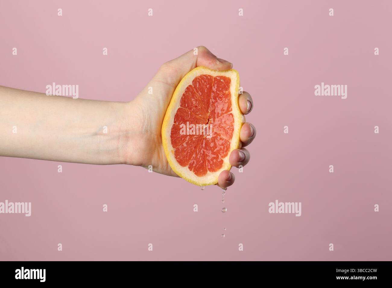 Woman squeezing grapefruit on pink background, closeup Stock Photo