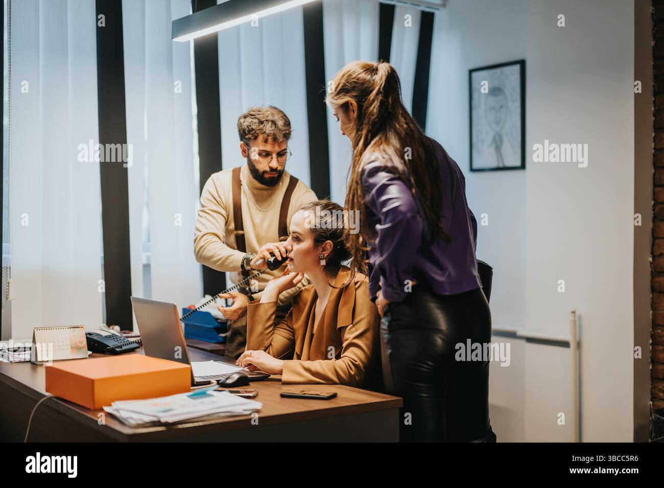 Three colleagues collaborating on a project in a modern office environment Stock Photo