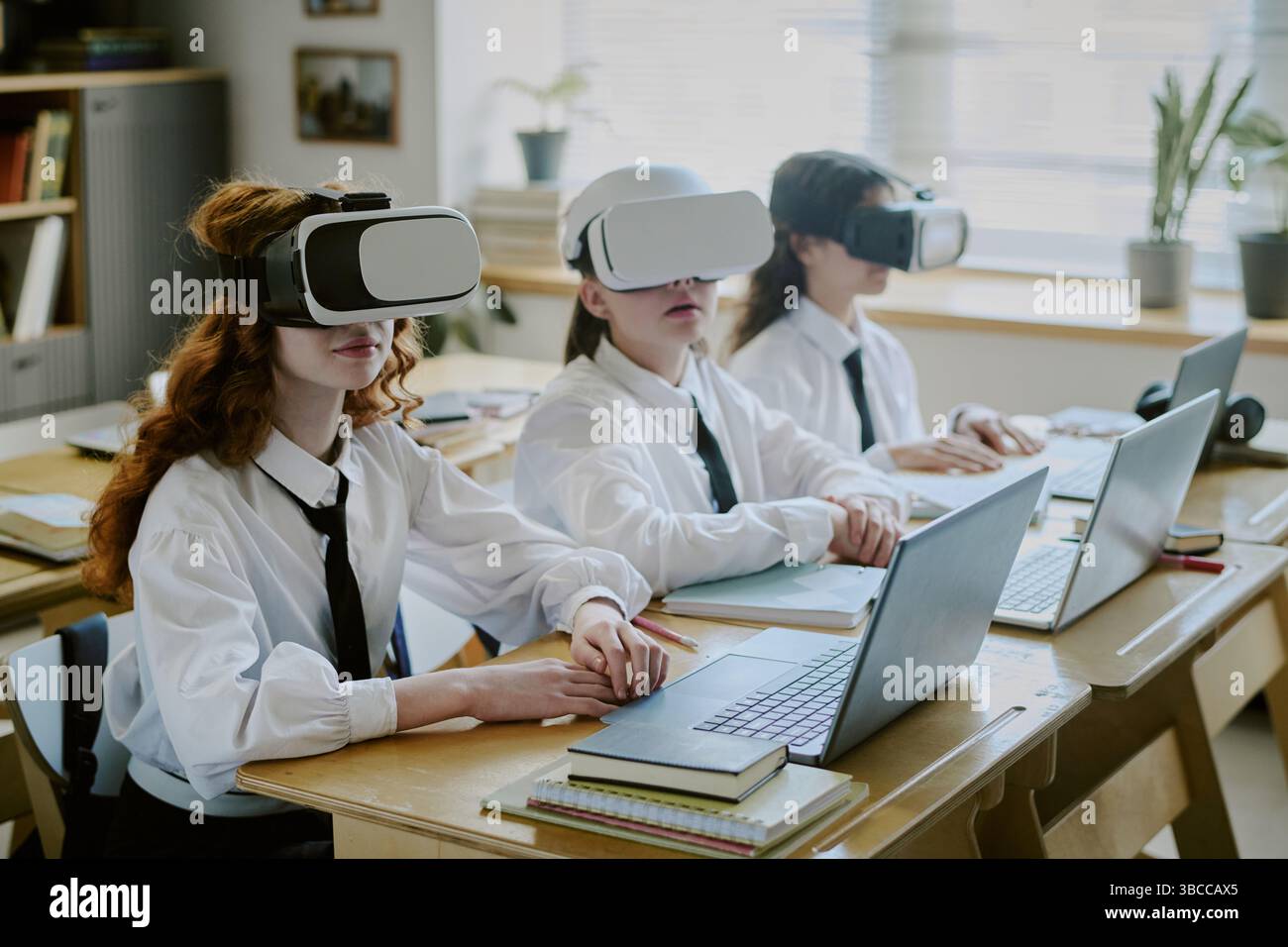 Students wearing virtual reality headsets and using laptops at classroom desk. Engaging in interactive learning experience with technology enhancing e Stock Photo