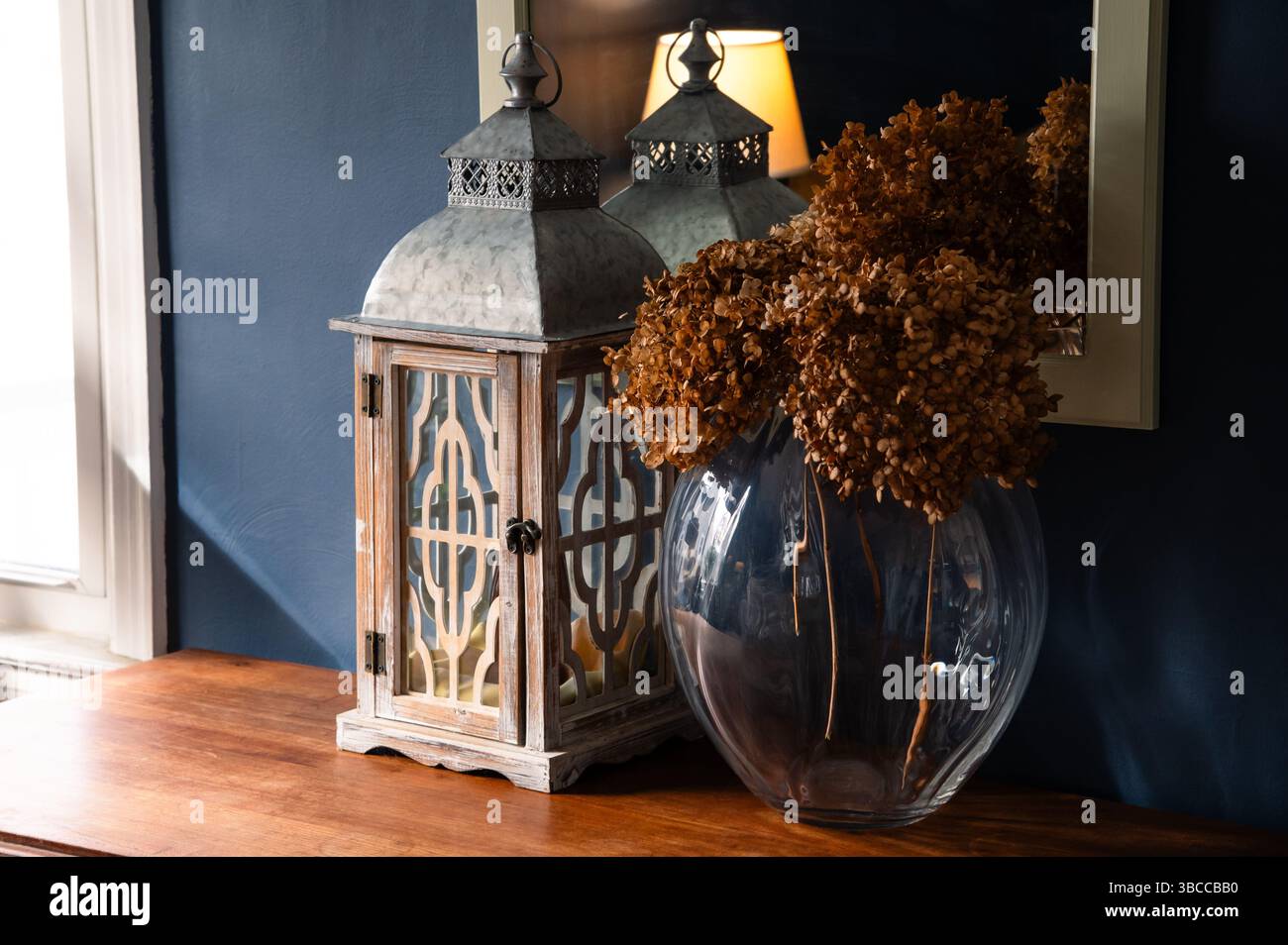 Dried hydrangea flowers and a white lantern on a wood console table in a blue room Stock Photo
