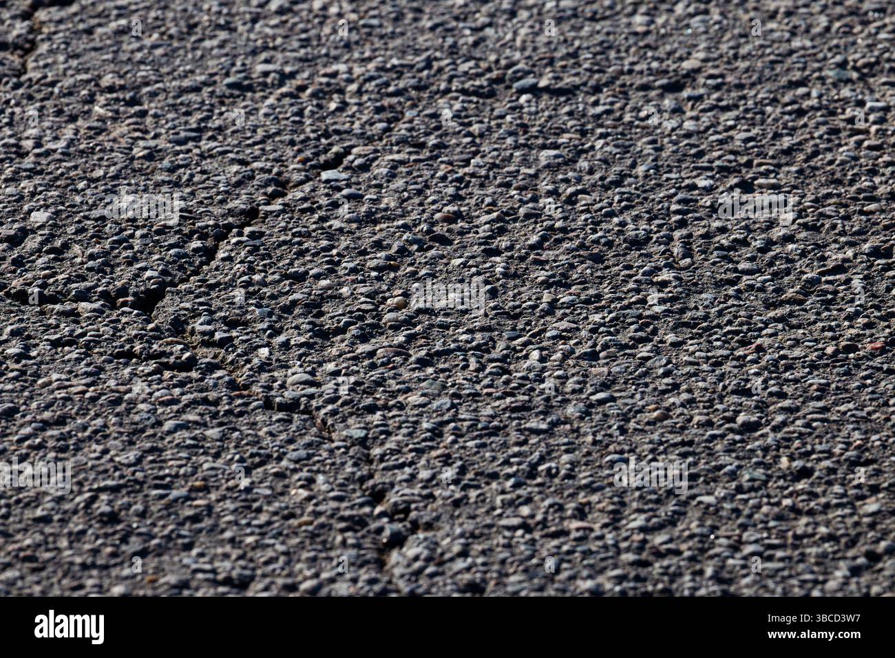 Close Up of Textured Asphalt Surface with Visible Cracks and Pebbles Stock Photo