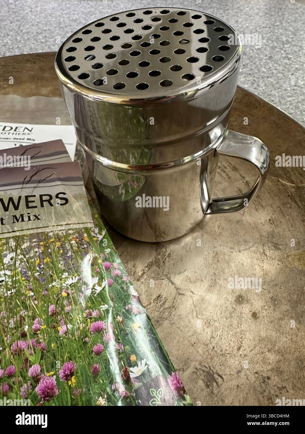A metal shaker with large holes and packets of wildflower seeds, for spreading seeds. Stock Photo