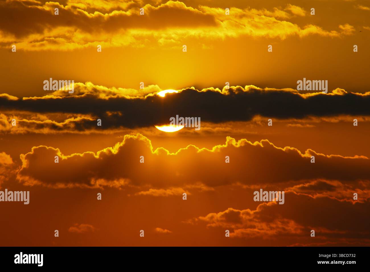 Stunning golden sunset with the sun partially hidden behind dramatic clouds, creating a warm and vivid sky perfect for nature and atmospheric themes. Stock Photo