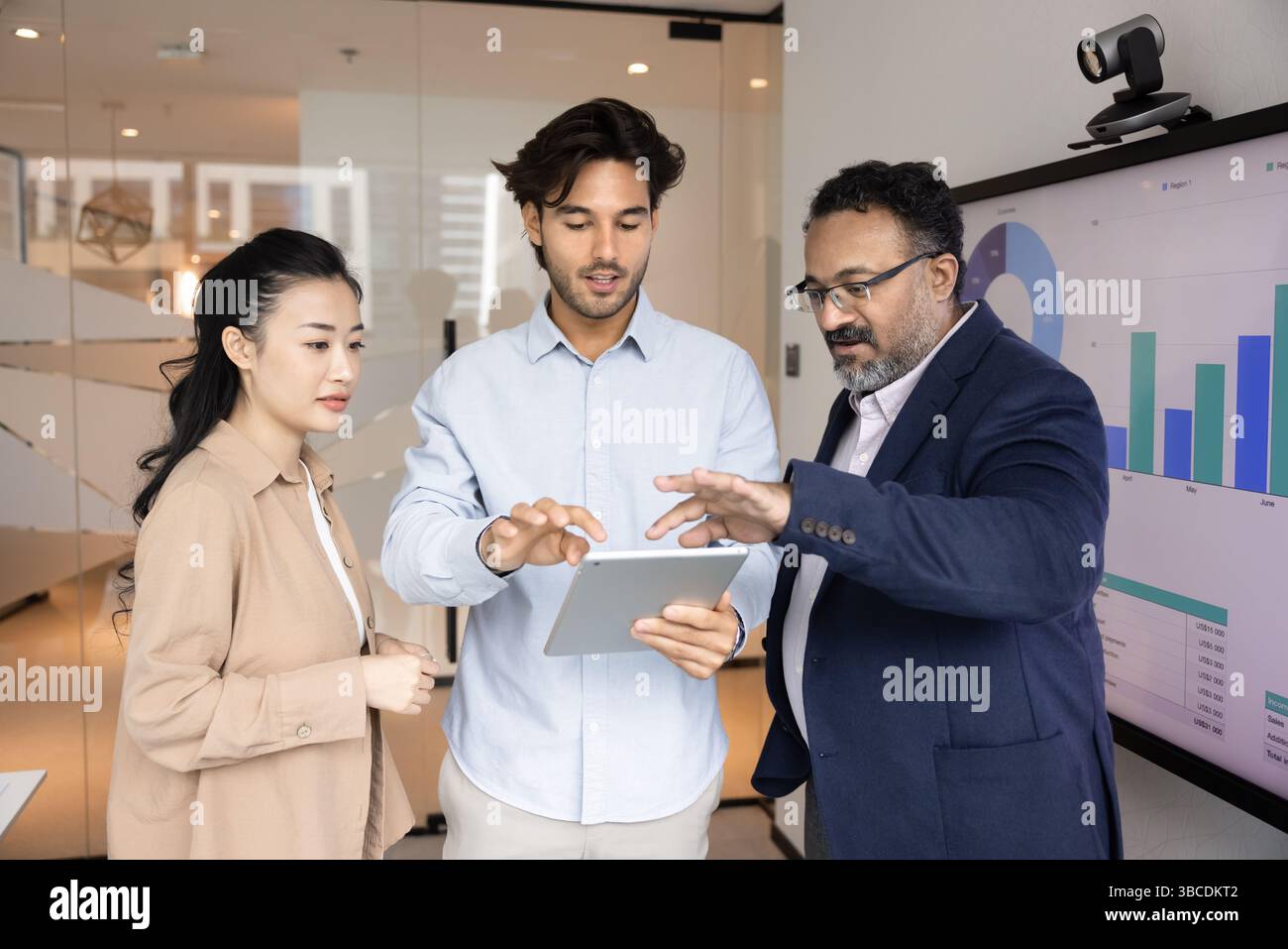 Teammates discussing data on tablet standing next to digital screen Stock Photo