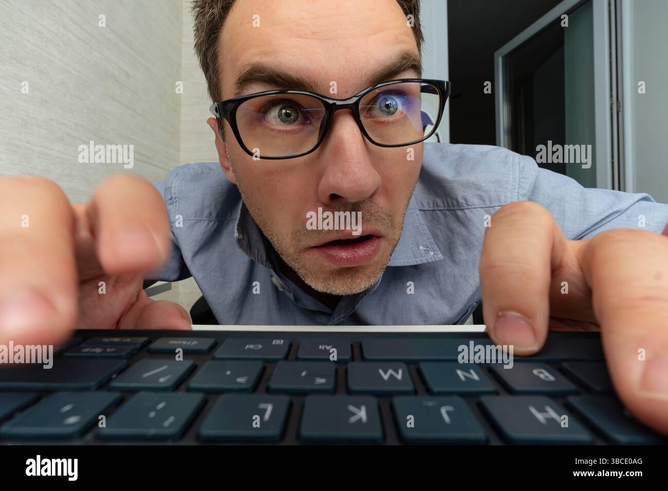 Young surprised copywriter geek software engineer IT specialist programmer man in blue shirt touch glasses work at office writing code type script on Stock Photo