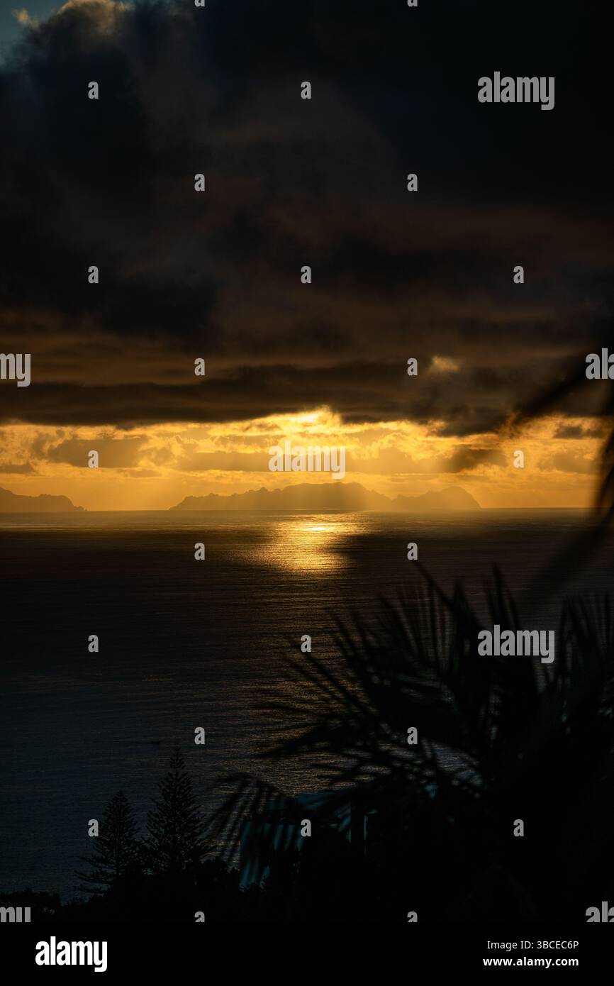 Dramatic sunset over the ocean with islands silhouetted against golden light and dark clouds Stock Photo
