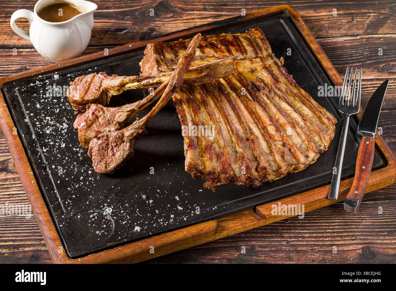Lamb racks grilled with herbs and sauce on a stone board Stock Photo