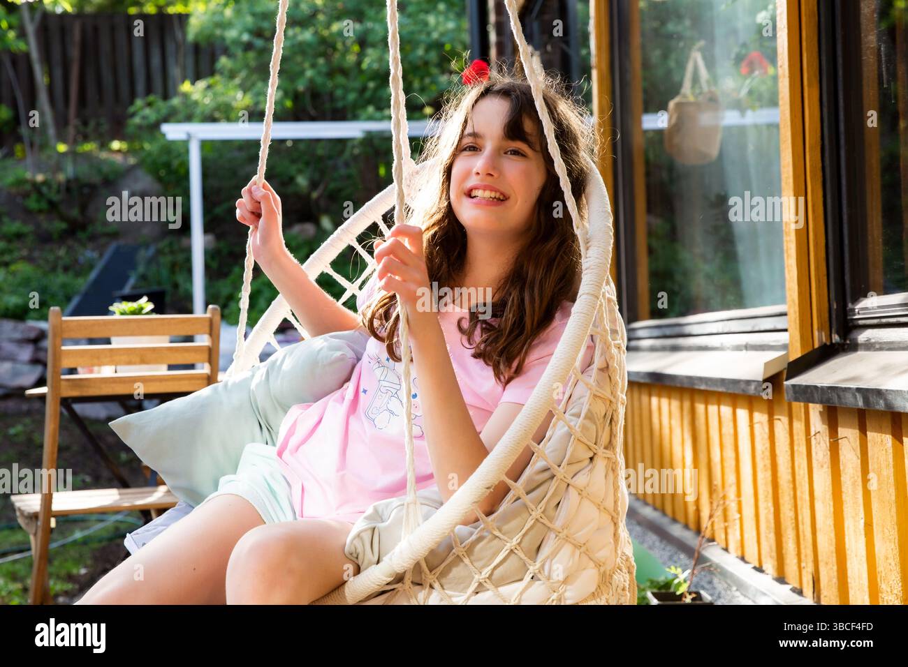 Tween girl happily swinging in a rope chair on the terrace of a private ...