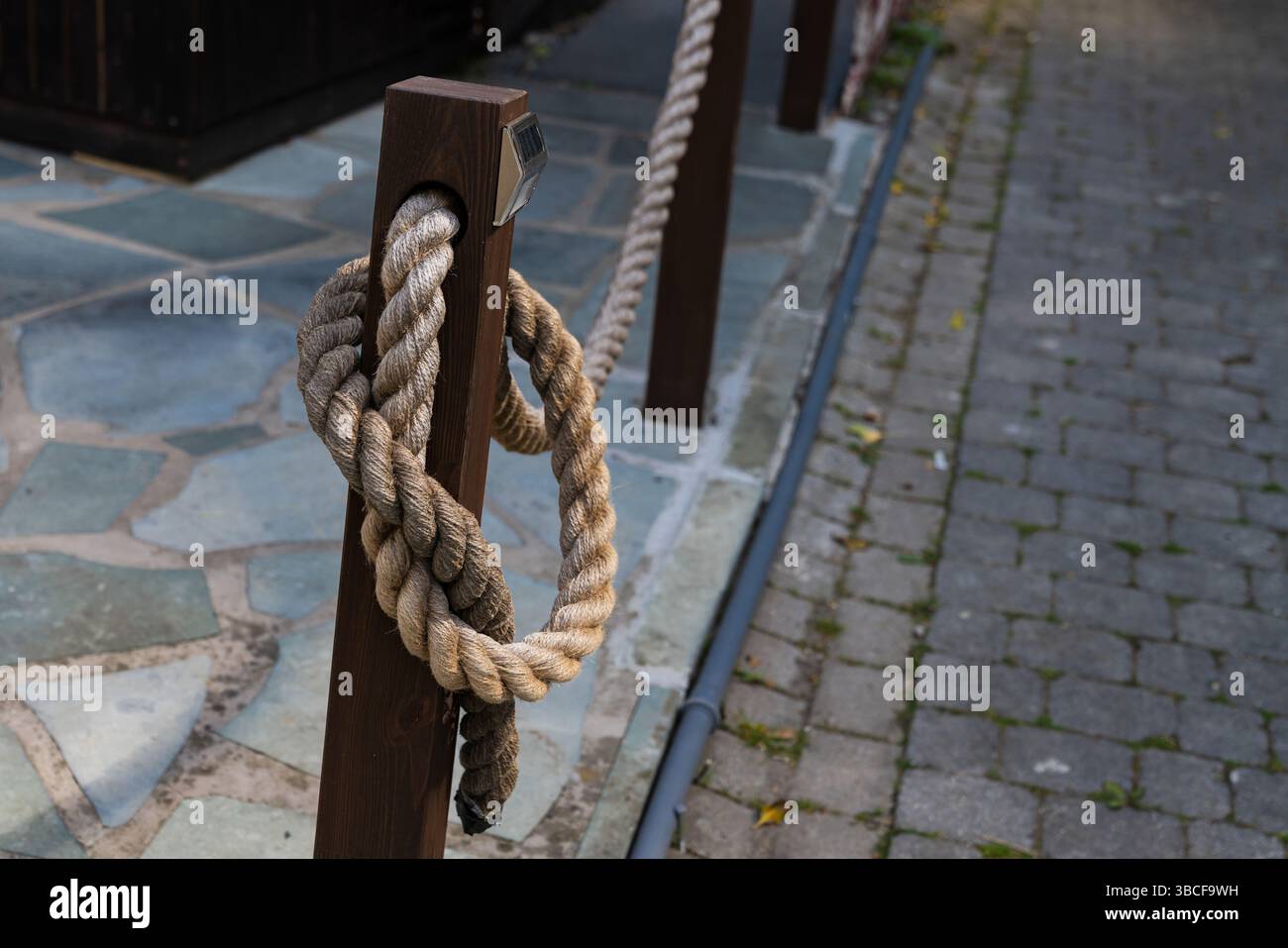 A thick rope is tightly coiled around a wooden post, standing beside a ...