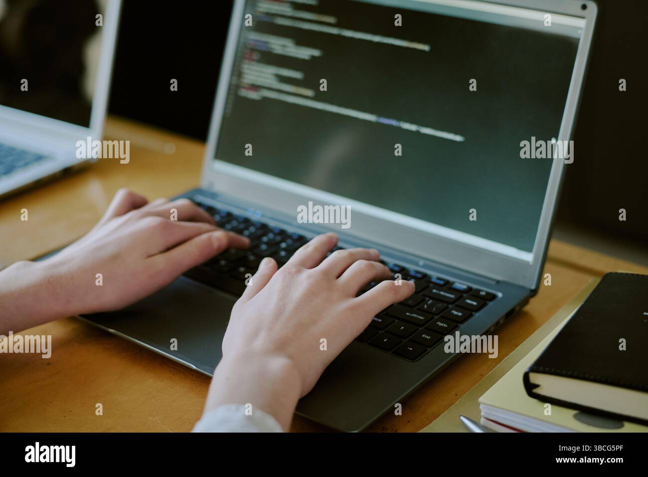 Close-up of hands typing code on laptop keyboard, with code visible on screen. Image focused on hands and coding activity, highlighting programming pr Stock Photo