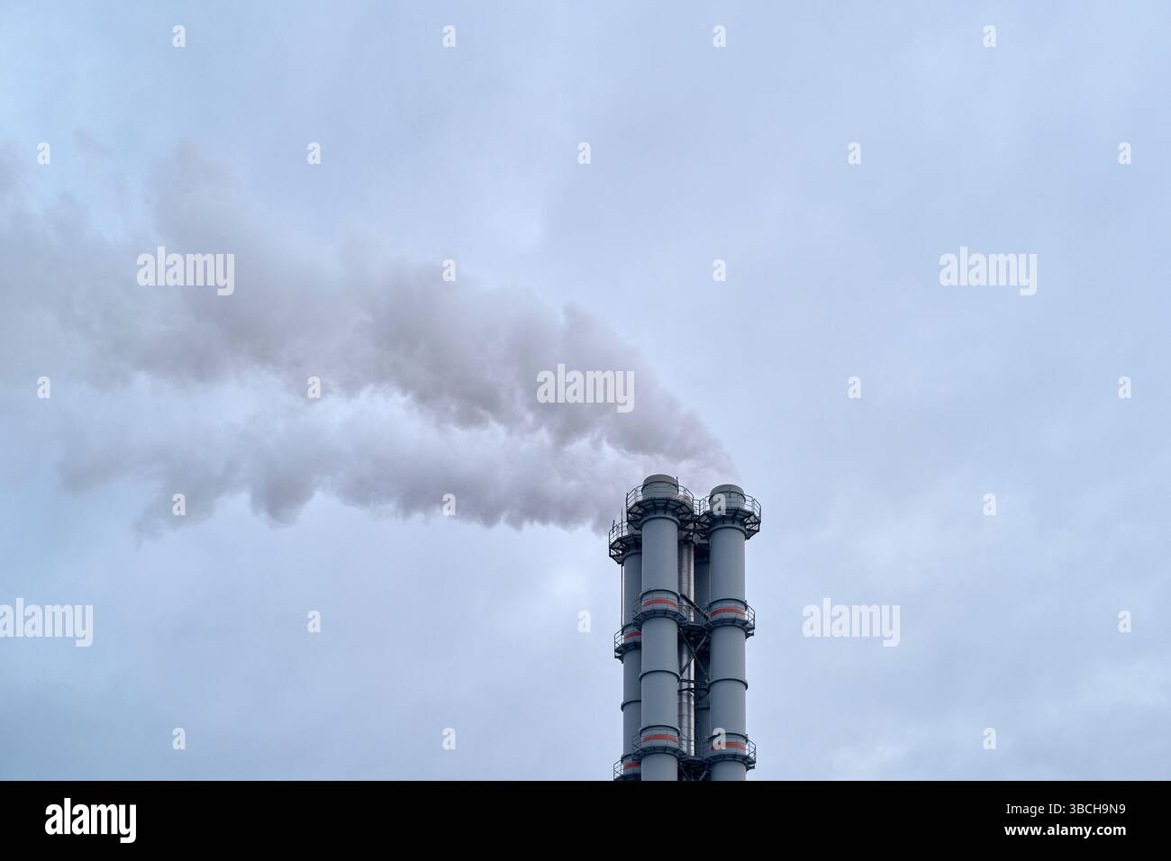 Industrial chimneys releasing smoke against a grey overcast sky ...