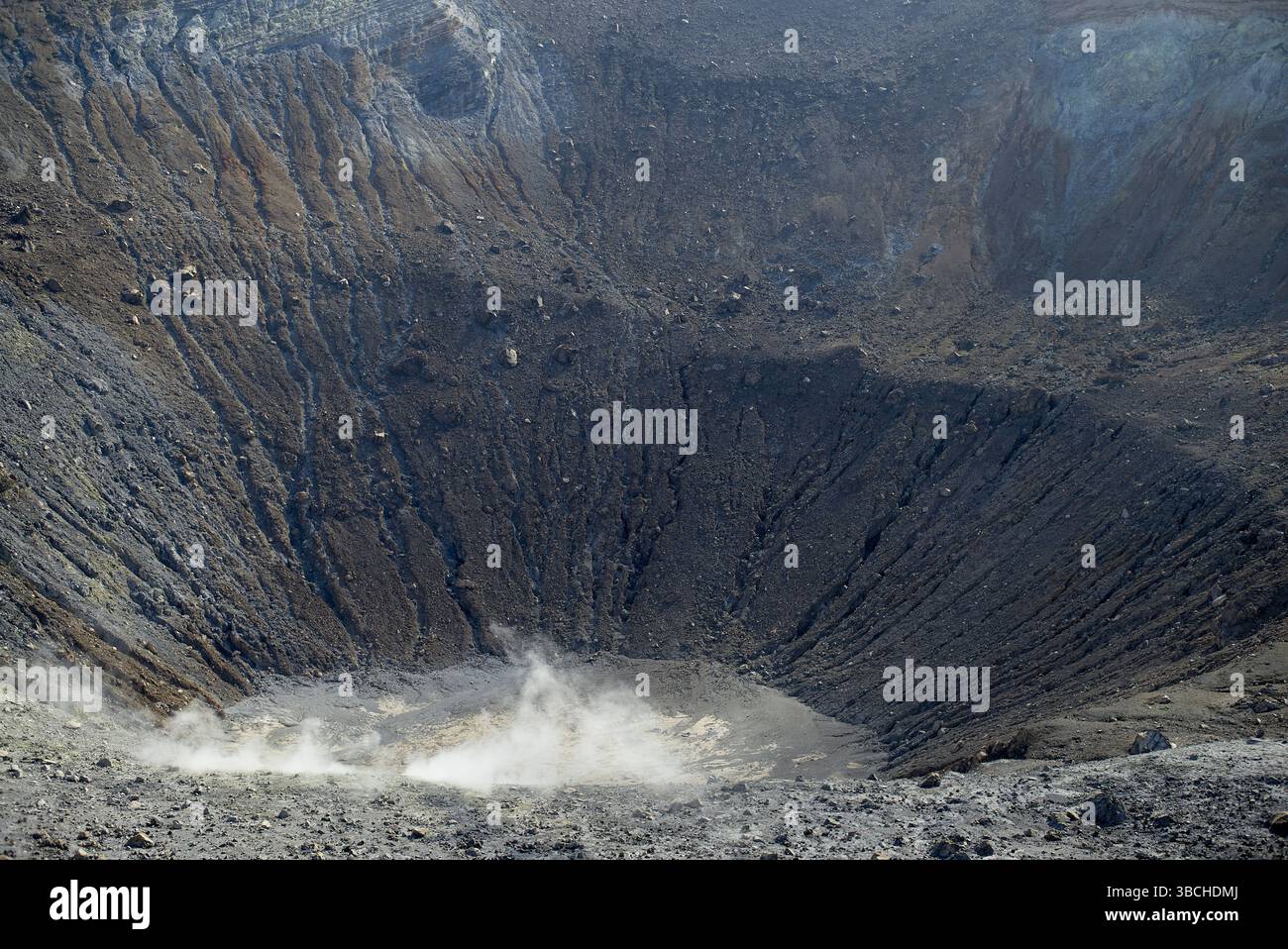 A rugged volcanic crater with steam rising from its barren, rocky surface in a desolate landscape. Sicily, Italy Stock Photo