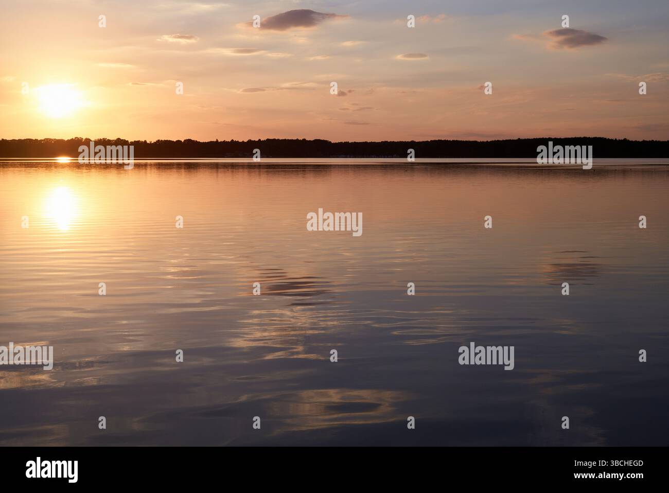 Sunset over a calm lake with reflections and soft clouds in the sky. Mecklenburg Lake Plateau, Germany Stock Photo