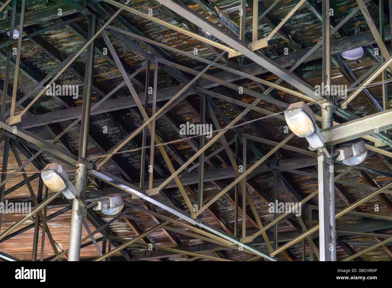 steel roof structure with industrial lights in an abandoned warehouse or factory. Rusted beams and damaged roofing indicate decay and neglect. Ideal f Stock Photo