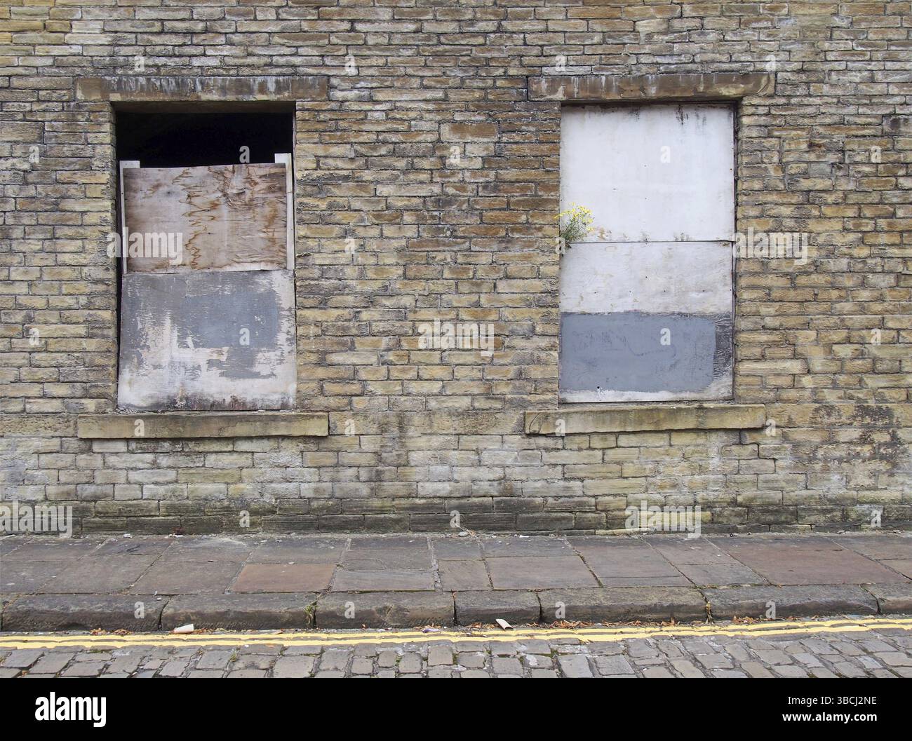Front view of an old abandoned derelict house on an empty street with boarded up windows and dilapidated brick walls Stock Photo